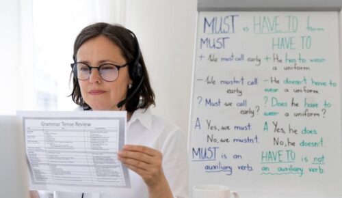 Online tutor holding grammar worksheet beside whiteboard