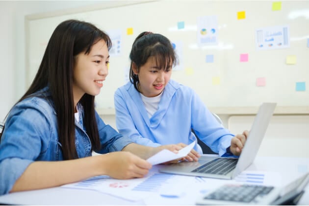 Two students collaborating on laptop and documents